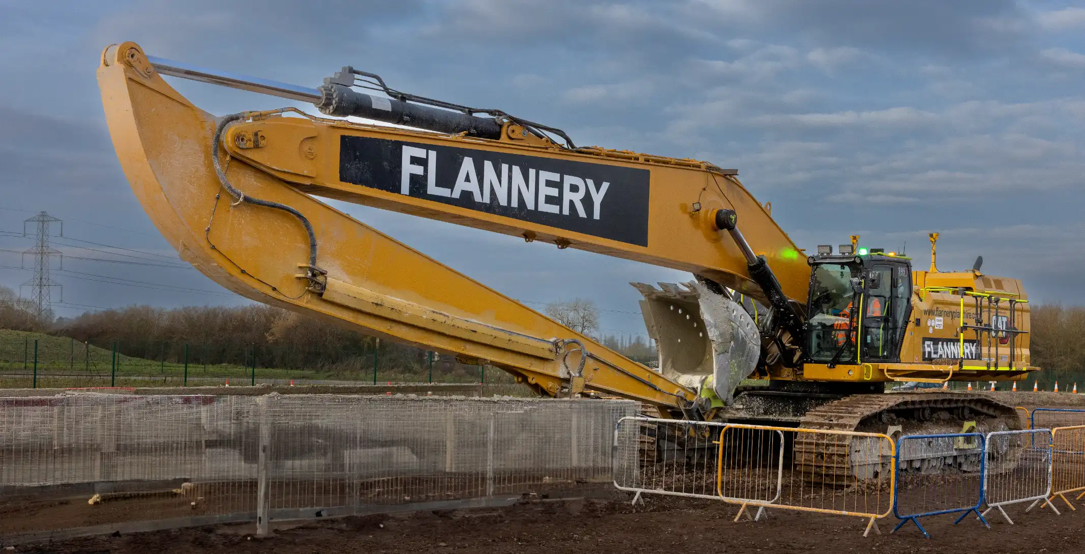 Excavator with a long reach arm on a construction site.